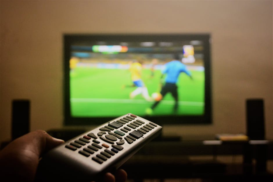 Hand holding remote with football match on TV screen